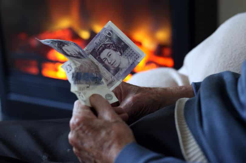 old person holding money in front of fire